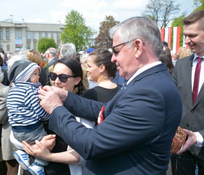 Marszałek województwa lubelskiego, Sławomir Sosnowski, przypina mieszkańcom biało-czerwone kokardki.