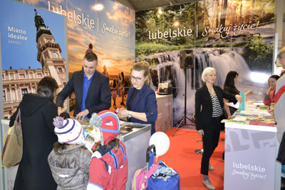 Grupa osób ogląda ulotki i materiały promujące województwo lubelskie na stoisku podczas targów Tour Salon