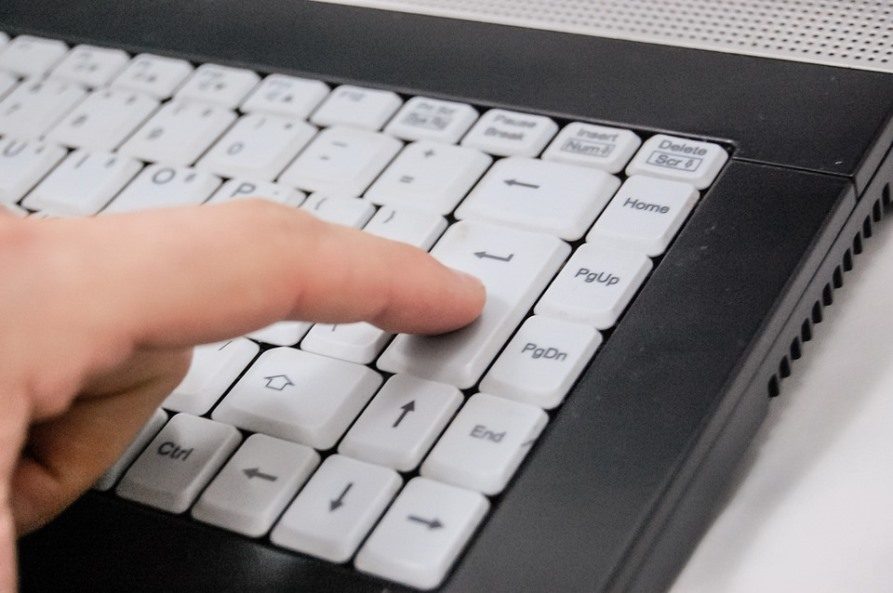 Na zdjęciu znajduje się dłoń pisząca na klawiaturze komputerowej