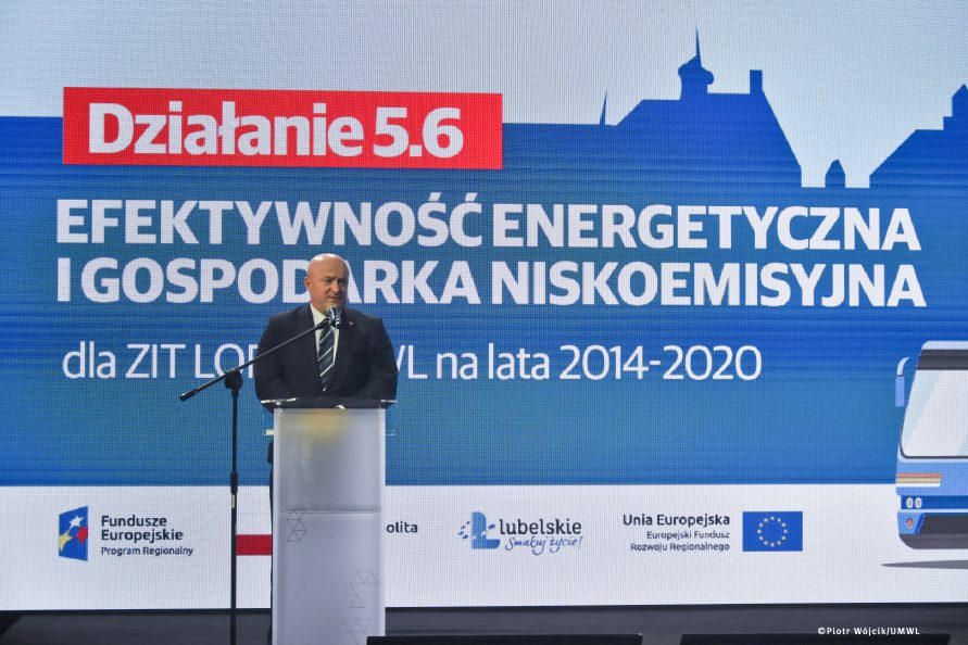 Marszałek Jarosław Stawiarski przy mównicy. W tle grafika działania 5.6 efektywność energetyczna i gospodarka niskoemisyjna.