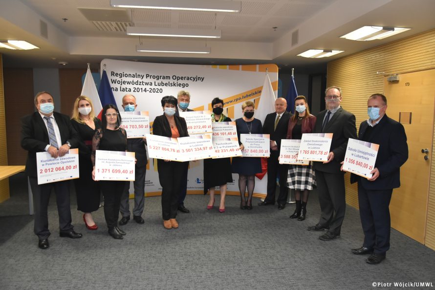 Grupowe zdjęcie beneficjentów z marszalkiem. Wszyscy beneficjenci trzymają symboliczne czeki z wypisanymi kwotami dofinansowania.