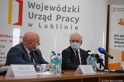Przy stole siedzą od lewej marszałek Jarosław Stawiarski, z prawej dyrektor Pruszkowski, na stole stoją mikrofony redakcji, w tle ścianka z logotypem i napisem Wojewódzki Urząd Pracy w Lublinie.