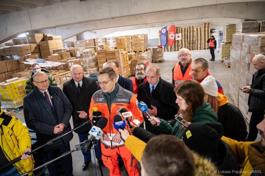 zdjecie przedstawia tłum osób, w centrum nich znajduje się ratownik medyczny, który udziela wypowiedzi do mikrofonu