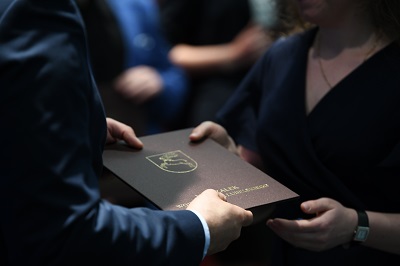 Dłonie dwóch osób podające sobie dokument zapakowany w twardą teczkę z wytłoczonym herbem województwa lubelskiego i napisem Marszałek Województwa Lubelskiego