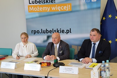 Dwóch meżcyzn i kobieta siedzą przy stole konferencyjnym za nimi plakat z napisem rpo.lubelskie.pl