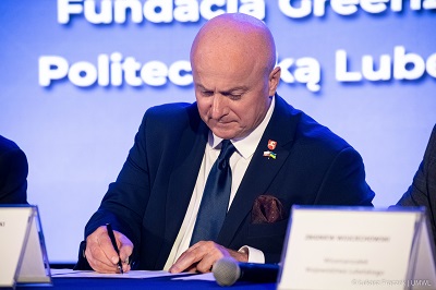 Marszałek Województwa Lubelskiego Jarosław Stawiarski podpisuje dokument, za nim ekran wyświetlający nazwę wydarzenia