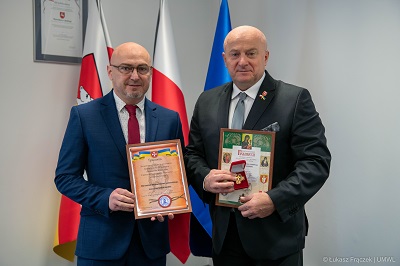 Marszałek WL wraz z gościem z Ukrainy pozuja do zdjęcia pokazująć oprawione dyplomy