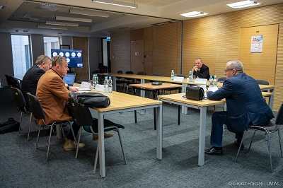 Posiedzenie zespołu, sala konferencyjna i czterech mężczyzn prowadzacych dyskusje