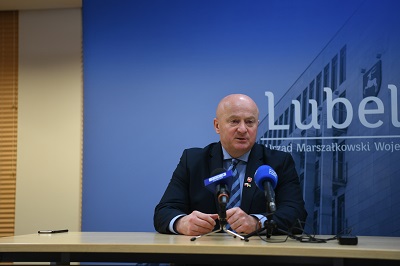 Marszałek Jarosław Stawiarski podczas konferencji prasowej. siedzi przy stole i udziela wypowiedzi, przed nim na stole ustawione dwa mikrofony
