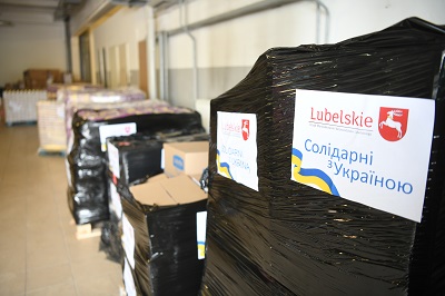 Pudła ustawione w garażu. Na każdym z nich znajduje się przyklejona naklejka z napisaem Lubelskie pomaga Ukrainie w jeżyku polskim i ukraińskim