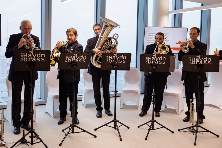 Czterech muzyków orkiestry dętej w trakcie gry na isntrumetnach, stoją przed partyrutami