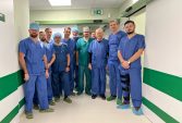 Około dziesięciu mężczyzn lekarzy chirurgów stoi w kitlach na korytarzu szpitala