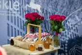 Stolik, na którym stoi koszyk z produkatmi regionalnymi oraz dwa wazony z różami