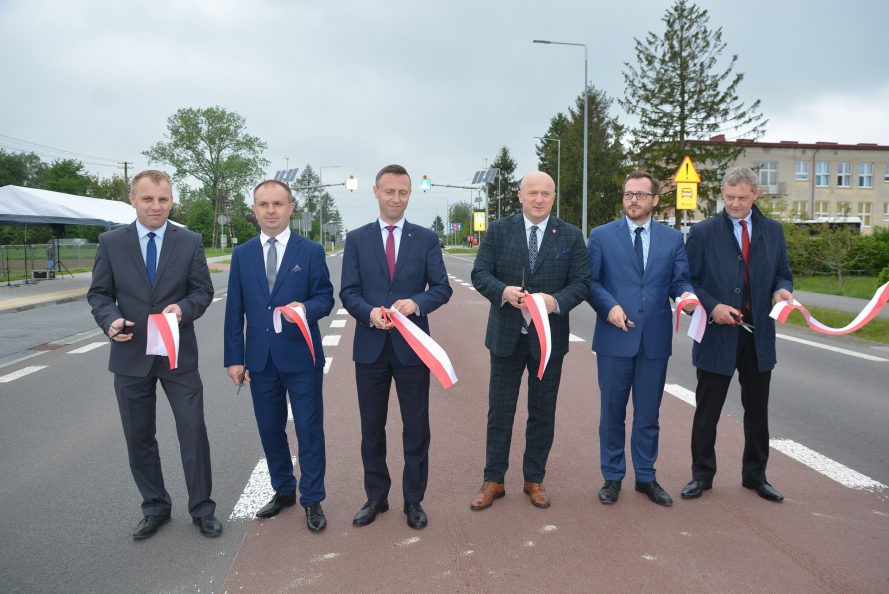 Sześciu mężczyzn stoi na nowo wybudowanej drodze wojewódzkiej. Wszyscy trzymają w rękach kawałki bialoczerwonej flagi i nożyczki
