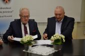 Dyrektor WSS im. Kardynała Stefana Wyszyńskiego i przedstawiciel fimy MaxBud podpisują wspólnie umowę. Obaj siedzą przy stole a przed nimi stoją dwa wazony z kwiatami