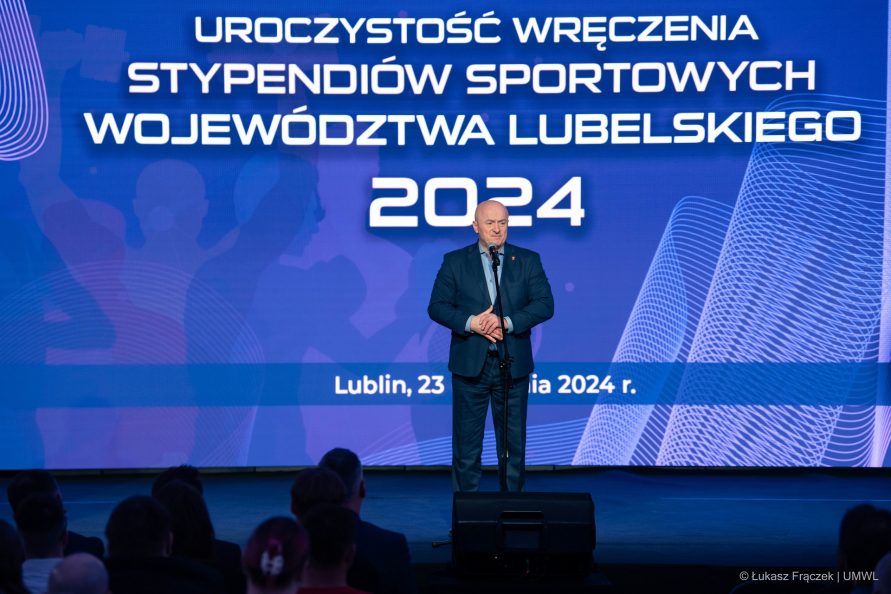Marszałek Jarosław Stawiarski stoi na scenie a zanim na ekranie wyświetla się napis Uroczystość wręczenie stypendiów sportowych województwa lubelskiego 2024