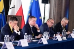Na zdjęciu widoczni są czterej elegancko ubrani mężczyźni, którzy siedzą za stołem nakrytym niebieskim suknem. Pierwszy z nich od lewej strony to Zdzisław Szwed, Członek Zarządu Województwa Lubelskiego. W tle widoczne są trzy flagi na stojakach, flaga Województwa Śląskiego, flaga Polski oraz Unii Europejskiej.