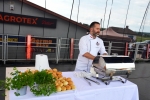 Zdjęcie przedstawia scenę i odbywający się na niej pokaz kulinarny Piotra Huszcza, który reprezentuje swoje danie: żeberka i bułeczki gryczane