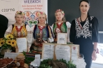 kobiety w strojach ludowych na stoisku promocyjnym trzymające nagrodę Perła 2023 i dyplom