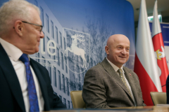 Piotr Matej oraz Jarosław Stawiarski siedzący razem przy jednym stoliku. Uśmiechają się patrząc na siebie i w głąb pomieszczenia. Za nimi widoczne są flaga Polski oraz flaga Województwa Lubelskiego.