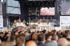 Biskup pomocniczy Archidiecezji Lubelskiej ksiądz Artur Miziński podczas odprawianej mszy dożynkowej. Zdjęcie wykonane z oddali pokazuje las głów wsłuchujących się w słowa księdza.