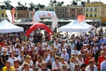 Zdjęcie przedstawia plan ogólny uczestniczących w imprezie gości. Wiele spośród osób na zdjęciu ubranych jest w stroje ludowe. W tle widać kamienice zamojskiego rynku i namioty wystawców. Jest piękna pogoda