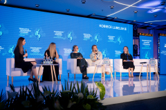 Panel dyskusyjny Kobiece Lubelskie. Pięć kobiet siedzi w białych fotelach na scenie, a jedna z uczestniczek wypowiada się do mikrofonu