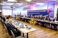 Zdjęcie dużej sali. Po dwóch stronach naprzeciwko siebie ustawione są stoliki z krzesłami, przy których siedzą Marszałkowie Polskich Województw. Pod jedną ze ścian stoi granatowa ścianka z napisem: „Konwent Marszałków Województw RP, Małopolska 2025”. Na jednej ze ścian wisi rozwijany ekran, na którym wyświetlana jest prezentacja multimedialna.