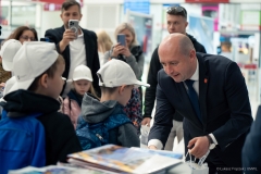 Wicemarszałek Piotr Breś przekazuje pakiet z gadżetami małemu chłopcu, obok czeka w kolejce kilkoro innych dzieci