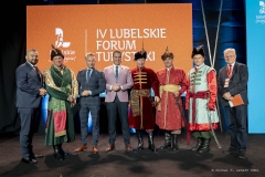 Kobieta stoi na scenie i zwraca się do zebranych  za nią na dużym ekranie wyświetla się zdjęcie