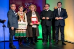Na scenie stoi kilka osób, na pierwszym planie znajdują się laureaci medalu, ubrani w stroje ludowe