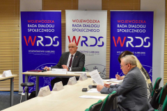 Posiedzenie Stałego Zespołu Roboczego ds. Rynku Pracy, Zatrudnienia, Wynagrodzeń i Świadczeń Socjalnych WRDS WL . Przy  stole konferencyjnym siedzi kilka osób.  W centralnym miejscu siedzi Przewodniczący  zespołu, który prowadzi obrady.  W tle widoczne  są  trzy  roll-upy  z logo WRDS WL 