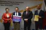 Przekazanie czeków na realizację działań związanych z przeciwdziałaniem skutkom rozprzestrzeniania się pandemii Covid-19 w domach pomocy społecznej. Od lewej: zastępca dyrektora ROPS Marta Drozd, Starosta Powiatu Biłgorajskiego Andrzej Szarlip trzyma czek z wypisaną kwotą dofinansowania, Marszałek Jarosław Stawiarski, Wicestarosta Biłgorajski Tomasz Rogala trzyma teczkę z umową dofinansowania.
