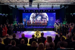 Widok na salę konferencyjną na której znajduje się kilkudziesięciu uczestników spotkania. Na scenie stoi zespół ludowy