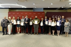 Członek Zarządu WL Marcin Szewczak pozuje do wspólnego zdjęcia ze stypendystami. Wszyscy stoją w sali konferencyjnej za nimi znajduje się ścianka lubelskie smakuj życie i 550 lecie województwa lubelskiego