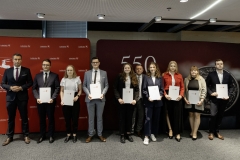 Członek Zarządu WL Marcin Szewczak pozuje do wspólnego zdjęcia ze stypendystami. Wszyscy stoją w sali konferencyjnej za nimi znajduje się ścianka lubelskie smakuj życie i 550 lecie województwa lubelskiego