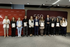 Członek Zarządu WL Marcin Szewczak pozuje do wspólnego zdjęcia ze stypendystami. Wszyscy stoją w sali konferencyjnej za nimi znajduje się ścianka lubelskie smakuj życie i 550 lecie województwa lubelskiego
