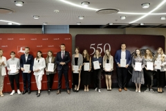 Członek Zarządu WL Marcin Szewczak pozuje do wspólnego zdjęcia ze stypendystami. Wszyscy stoją w sali konferencyjnej za nimi znajduje się ścianka lubelskie smakuj życie i 550 lecie województwa lubelskiego