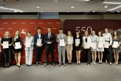 Członek Zarządu WL Marcin Szewczak pozuje do wspólnego zdjęcia ze stypendystami. Wszyscy stoją w sali konferencyjnej za nimi znajduje się ścianka lubelskie smakuj życie i 550 lecie województwa lubelskiego