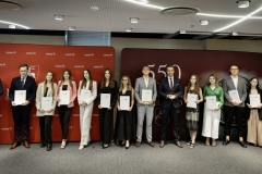 Członek Zarządu WL Marcin Szewczak pozuje do wspólnego zdjęcia ze stypendystami. Wszyscy stoją w sali konferencyjnej za nimi znajduje się ścianka lubelskie smakuj życie i 550 lecie województwa lubelskiego