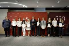 Członek Zarządu WL Marcin Szewczak pozuje do wspólnego zdjęcia ze stypendystami. Wszyscy stoją w sali konferencyjnej za nimi znajduje się ścianka lubelskie smakuj życie i 550 lecie województwa lubelskiego