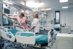 Dwie lekarki stoją przy łóżku szpitalnym i prezentują znajdującą się przy nim aparaturą
