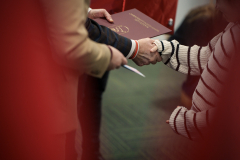 Zdjęcie przedstawiające ludzi ściskających sobie dłonie. Wśród nich jeden z nich trzyma teczkę.