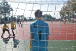 Mecz w ramach akcji "z podwórka na boisko".  W centralnej części kadru stoi plecami do obiektywu bramkarz w niebieskim stroju. widoczna jest siatka bramki. w tle rozgrzewający się zawodnicy