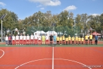 Mecz w ramach akcji "z podwórka na boisko". Grupowe zdjęcie zawodników, stojących na środku nowego boiska. po lewej zawodnicy urzędu w biało-czerwonych strojach. po prawej młodzież w zółto-czarnych strojach.