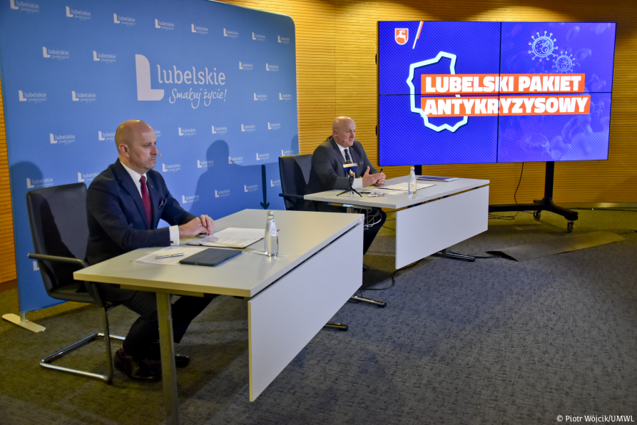 Na zdjęciu bliżej lewej krawędzi przy stole siedzi Dyrektor Wojewódzkiego Szpitala Spcejalistycznego w Białej Podlaskiej Adam Chodzinski. W głębi, również przy stole siedzi Marszałek Województwa Lubelskiego Jarosław Stawiarski. W tle ekran, na którym wyświetlana jest grafika Lubelski Pakiet Antykryzysowy