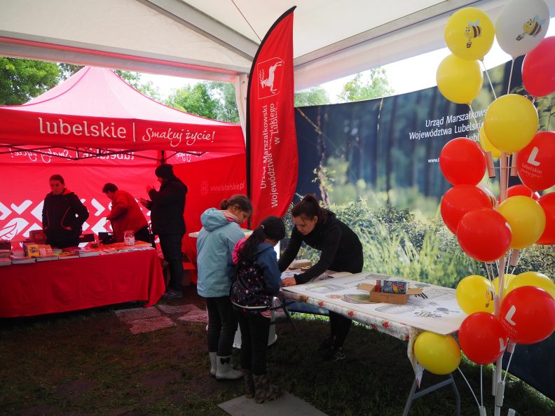 Zdjęcie przedstawiające wnętrze namiotu. Po prawe stronie przy stoliku stoją dwie dziewczynki i kobieta pokazująca im obrazki
