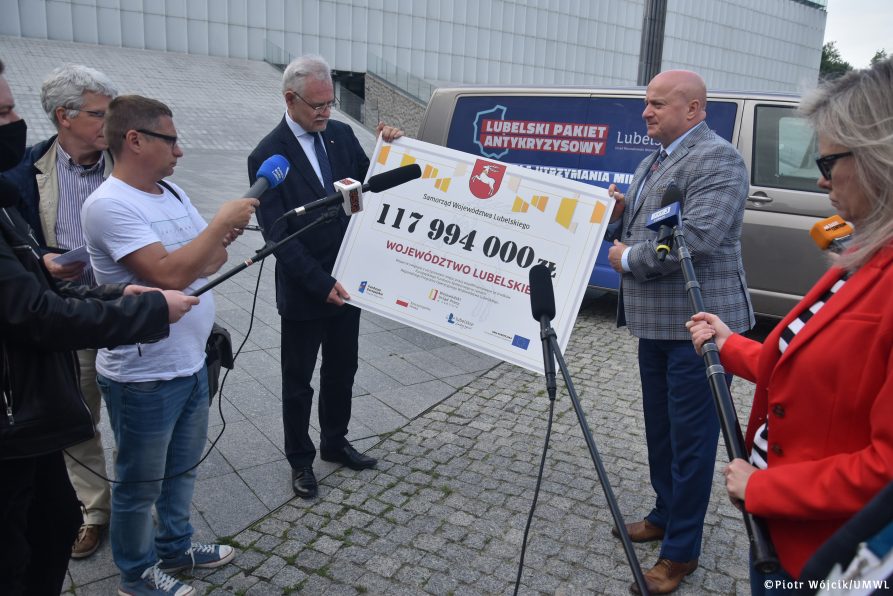 Dyrektor Wojewódzkiego Urzedu Pracy Andrzej Pruszkowski i Marszałek Województwa Lubelskiego Jarosław Stawiarski stoją przed oznakowanym busem Moblinego Punktu Informacyjnego trzymając tablicę, na której widnieje kwota 117 994 000 zł, które Samorząd Województwa Lubelskiego przekazał na Lubelski Pakiet Antykryzysowy.