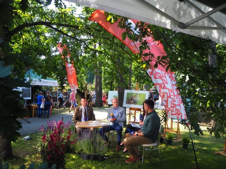 Zdjęcie przedstawiające trzech mężczyzn trzymających mikrofony i siedzących przy stoliku.