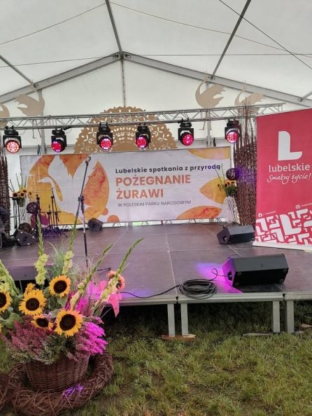 Zdjęcie przedstawiające pustą scenę a banerem z napisem Pożegnanie żurawi. Na pierwszym planie po lewej stronie znajduje się kosz wiklinowy ze słonecznikami